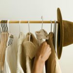 Stylish beige and brown clothes on a rack with a hand reaching in.